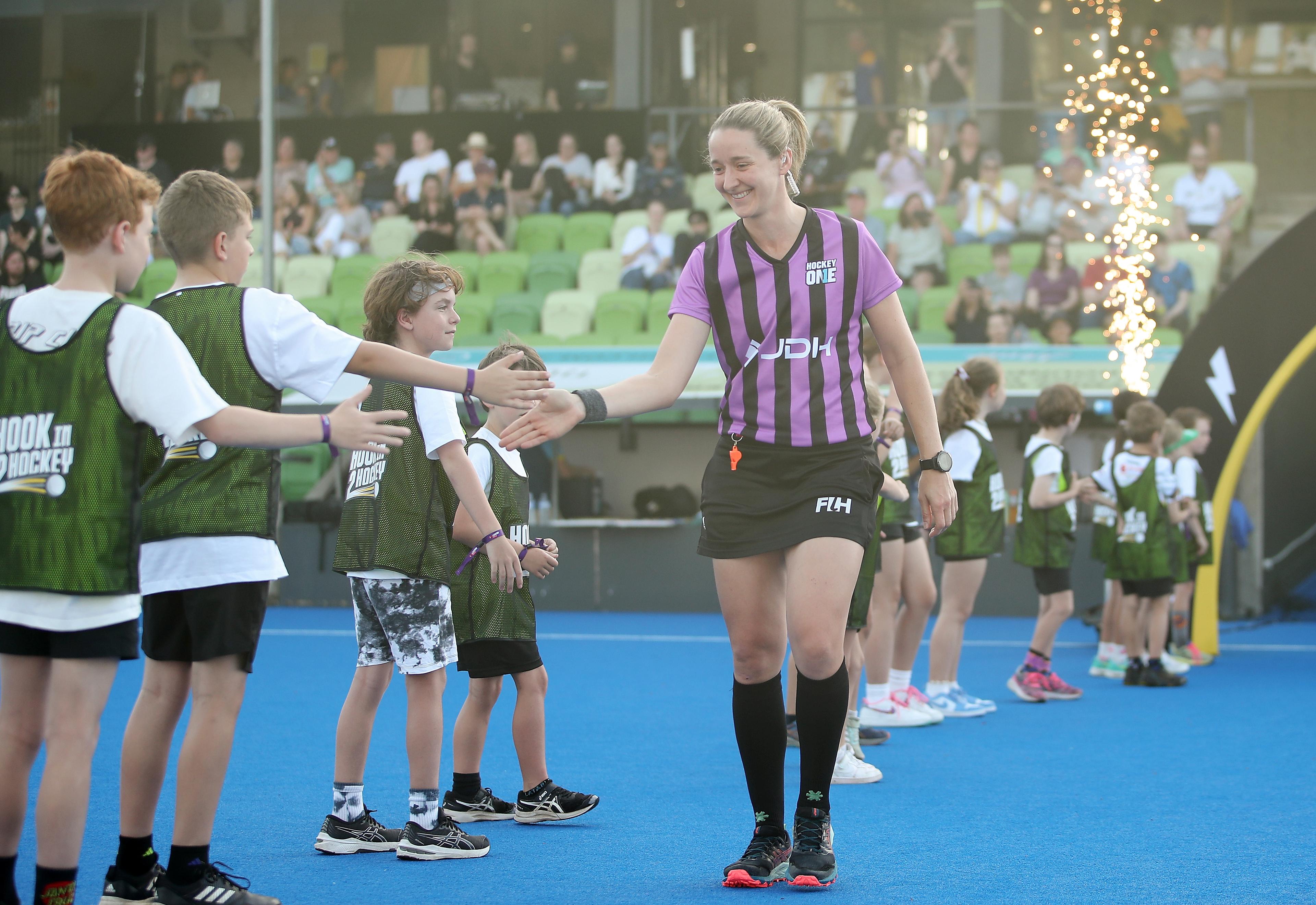 Aleisha Neumann is walking out onto a hockey pitch alongside a row of kids, and is giving one of the boys in the line a high five