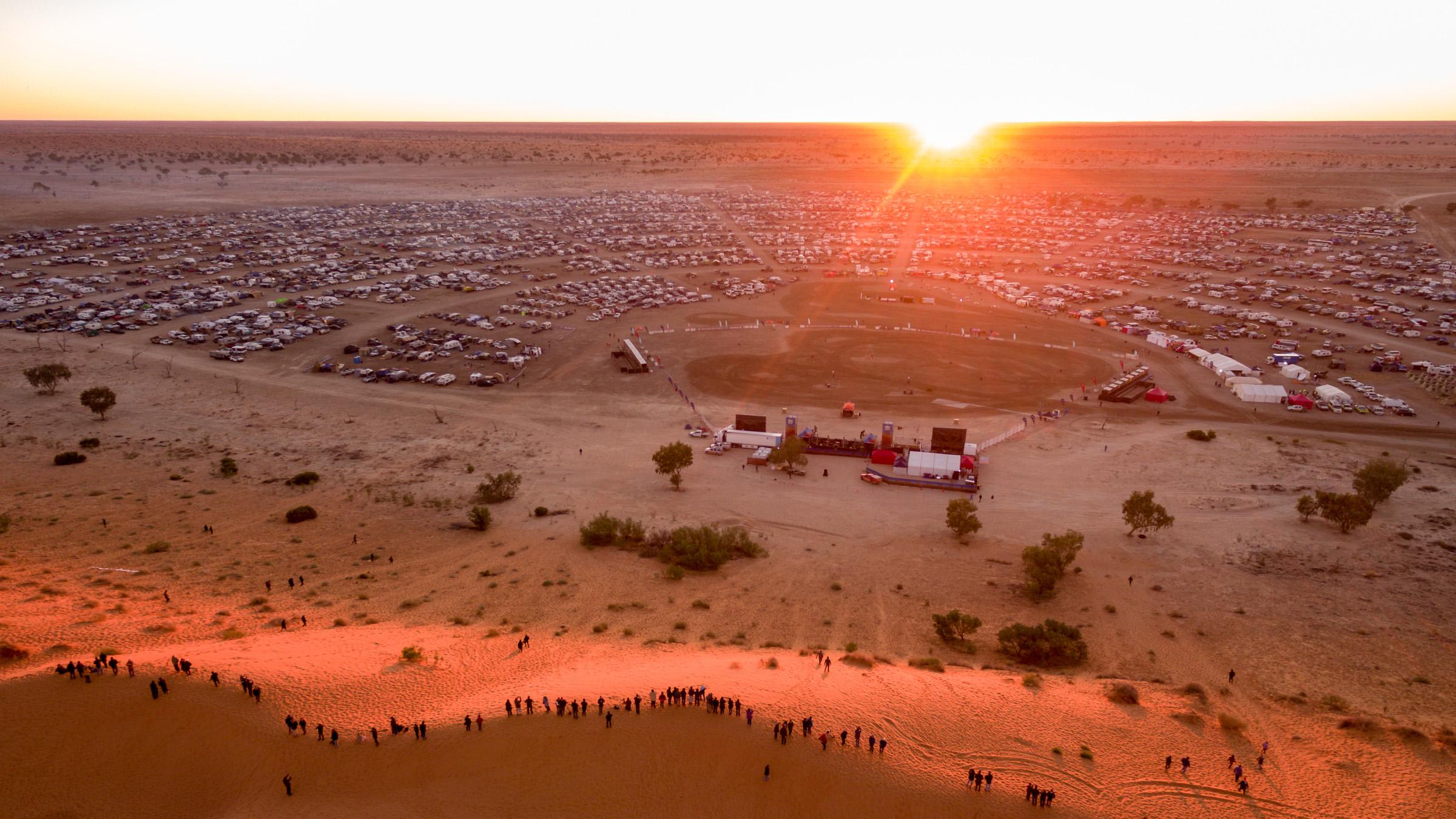 Aerial view of a festival stage in the desert with cars, camper vans and sand dunes