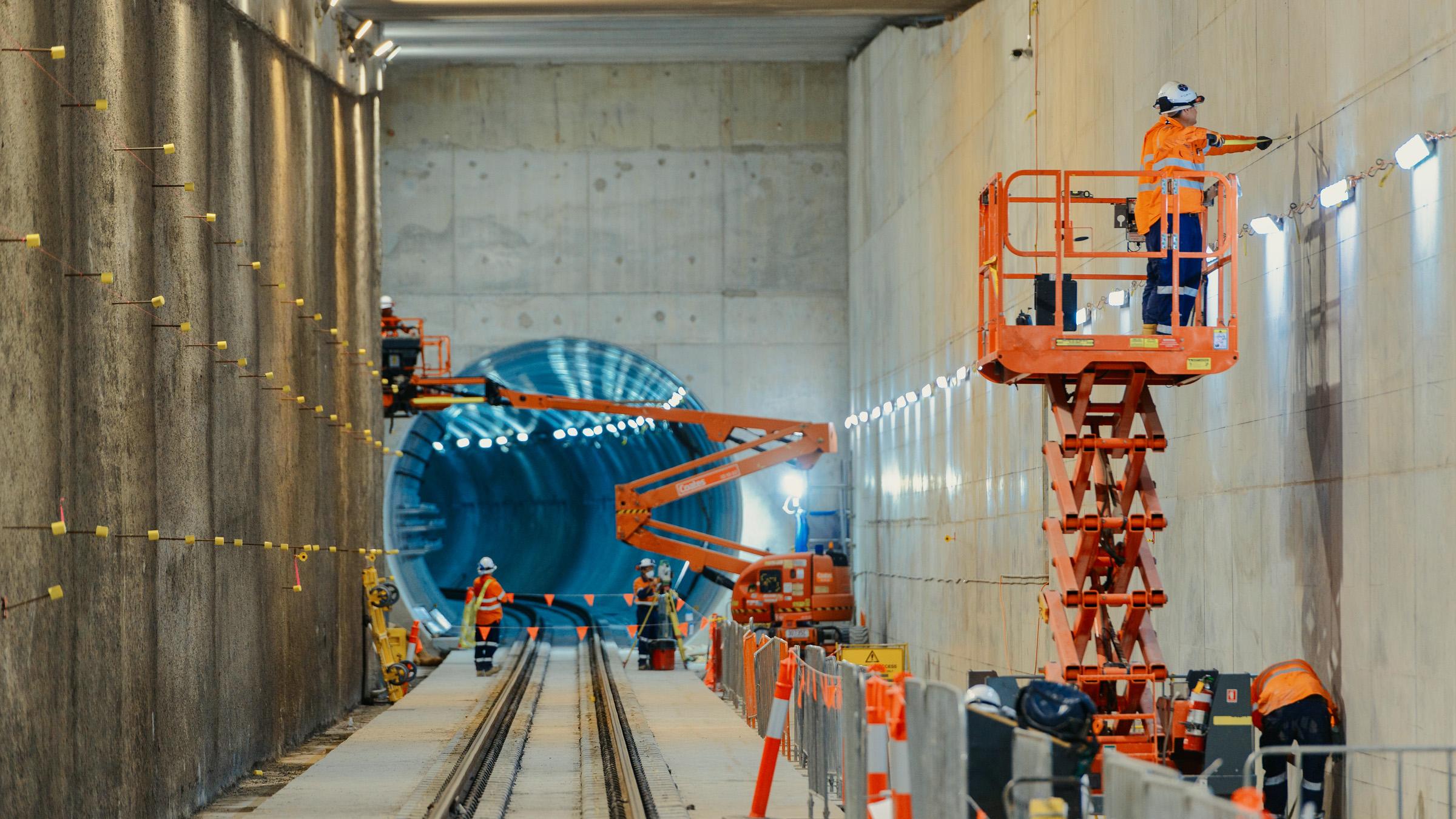 Construction crew in a Cross River Rail tunnel, inspecting the work on a scissor lift