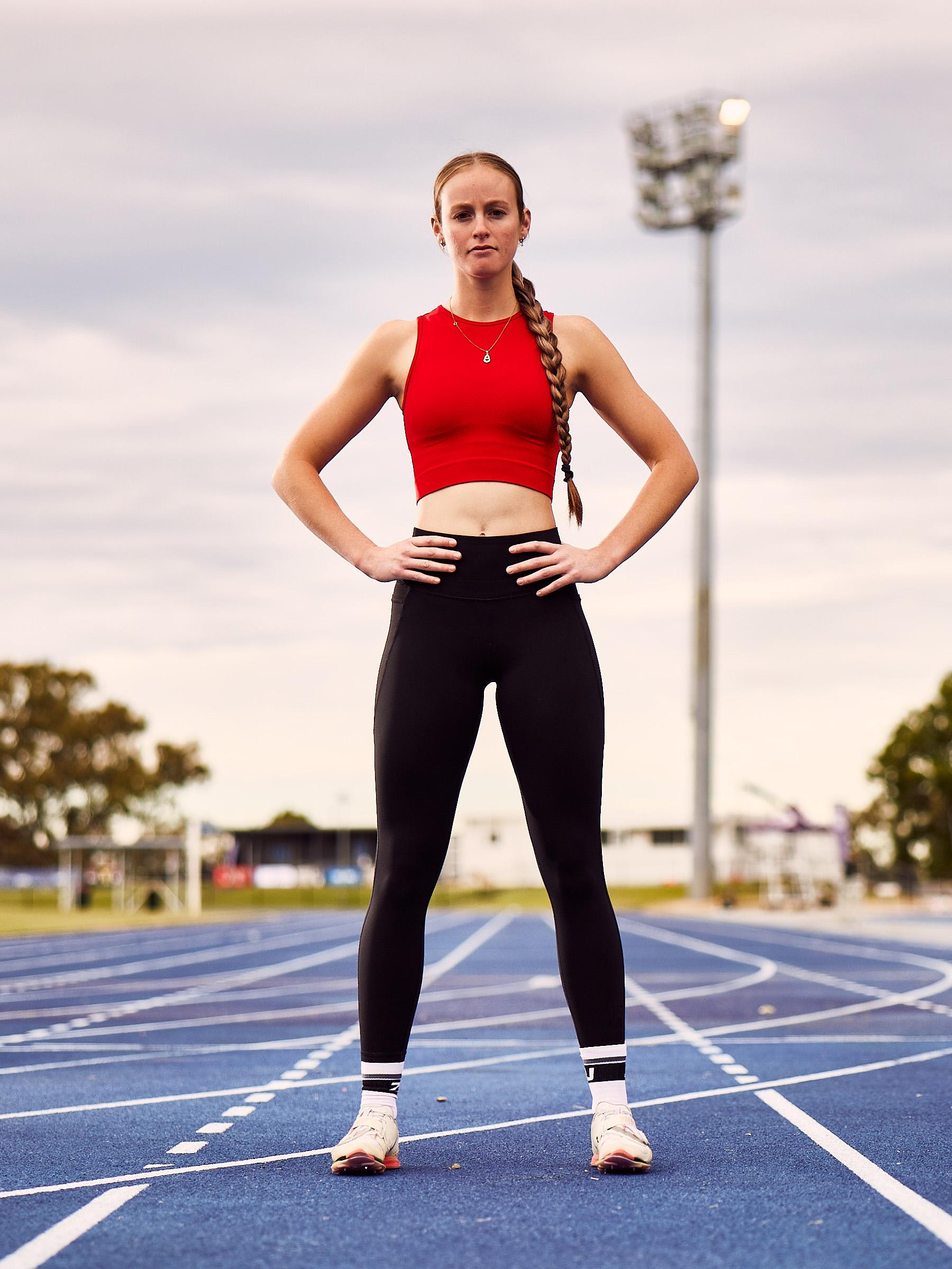 Young athlete in the middle of a blue track, standing strong with hands on hips