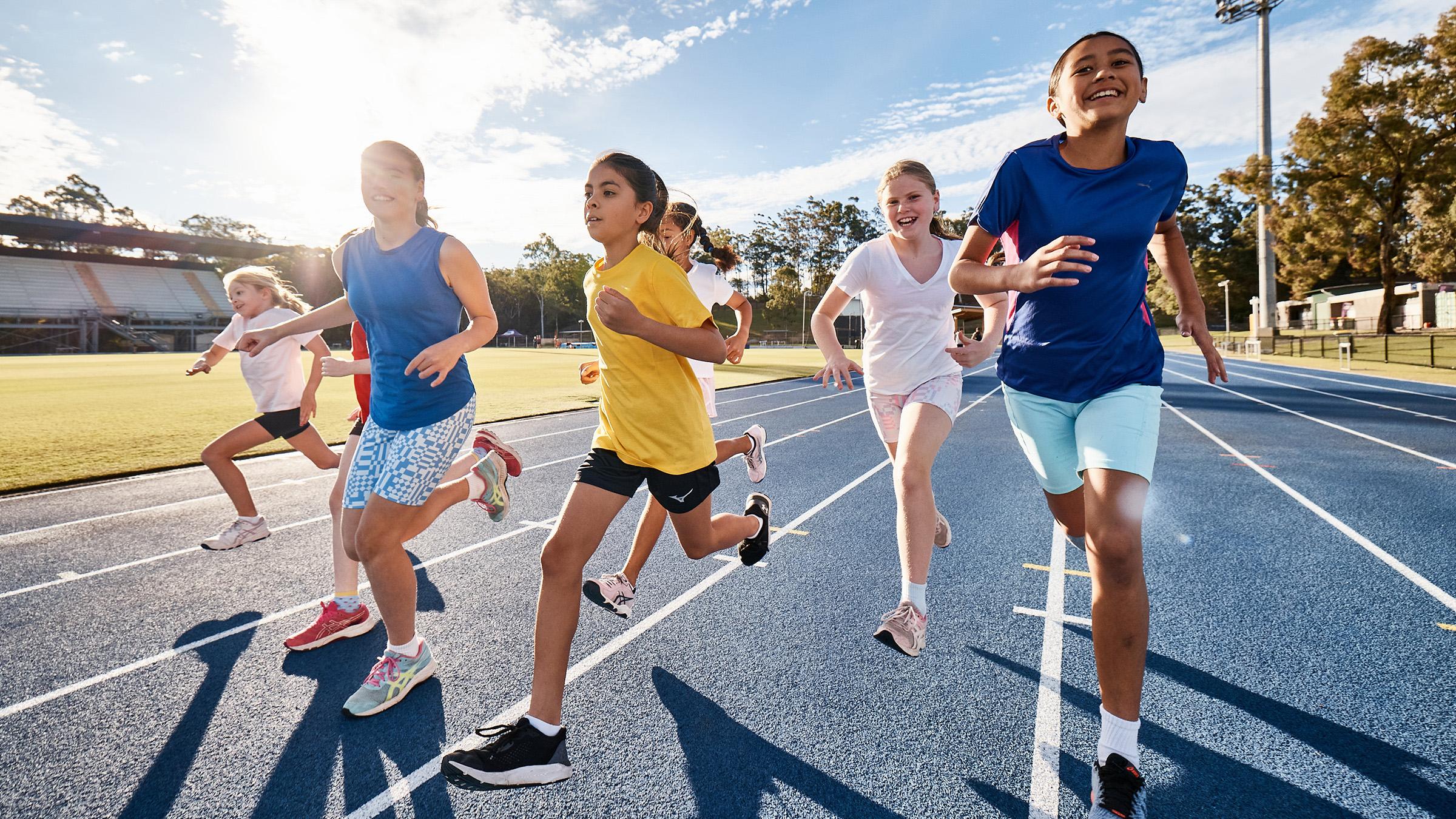 Children running on a blue athletics track on a sunny day