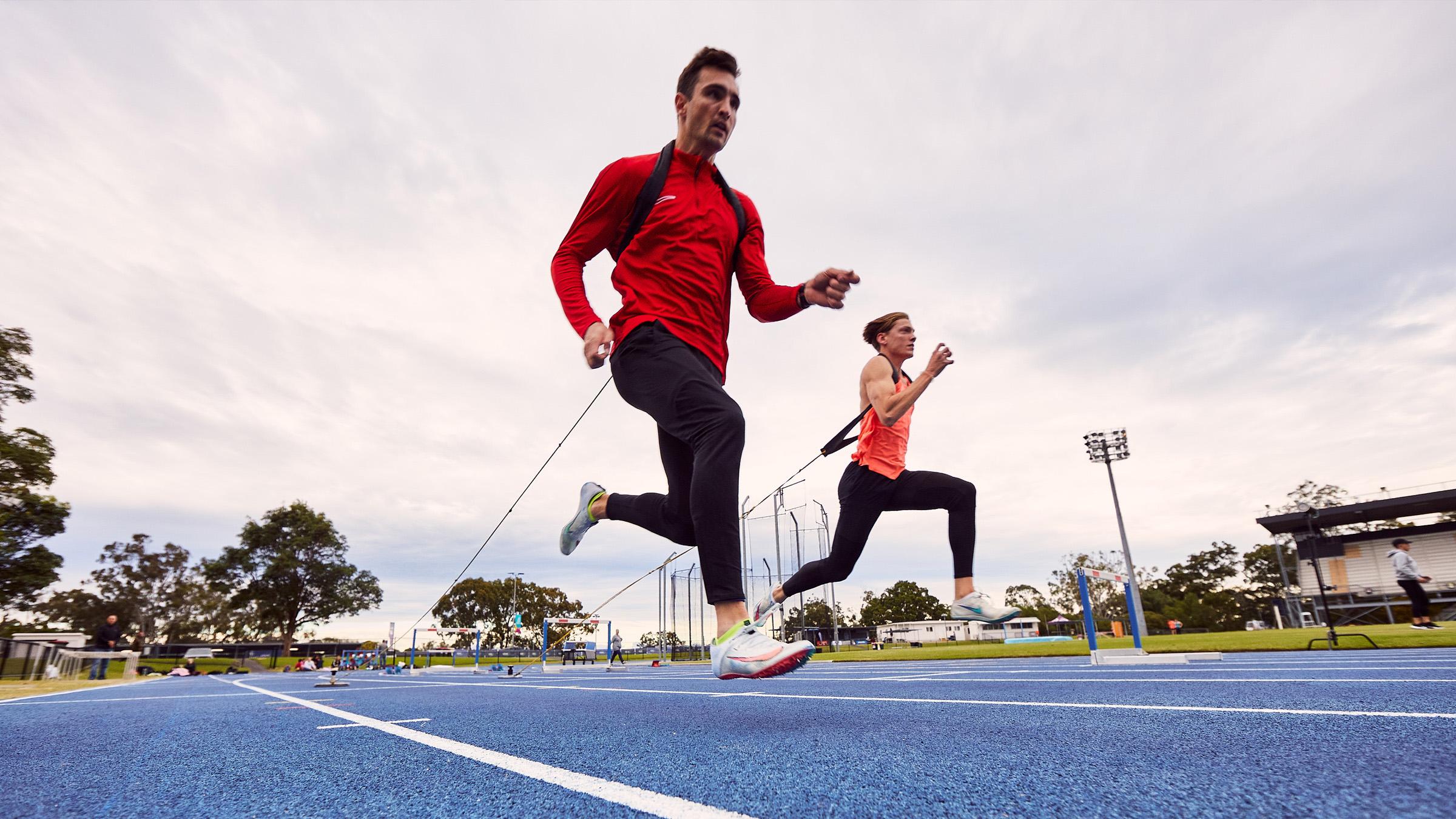 Two runners on a blue athletics track doing resistance training