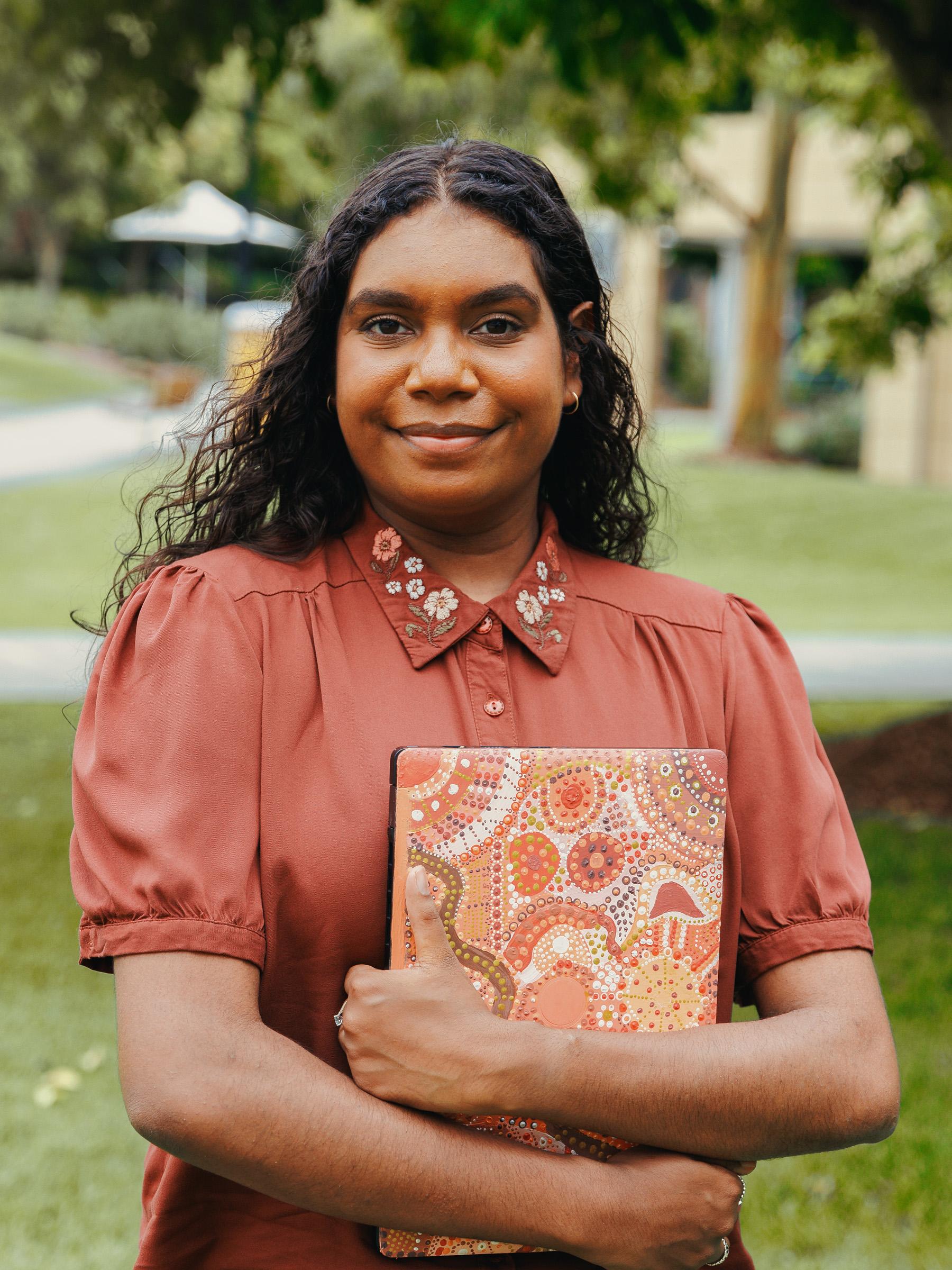 A young Aboriginal woman holding laptop covered in artwork they designed and painted