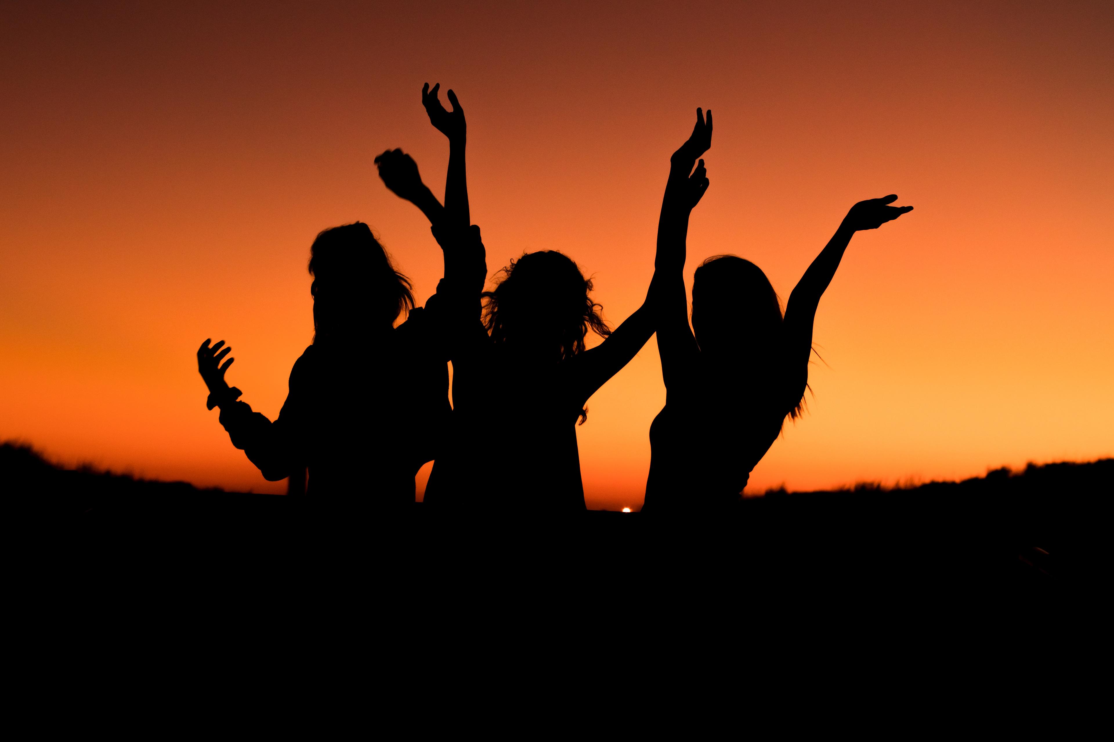 Three friends dancing with an orange sunset behind them.