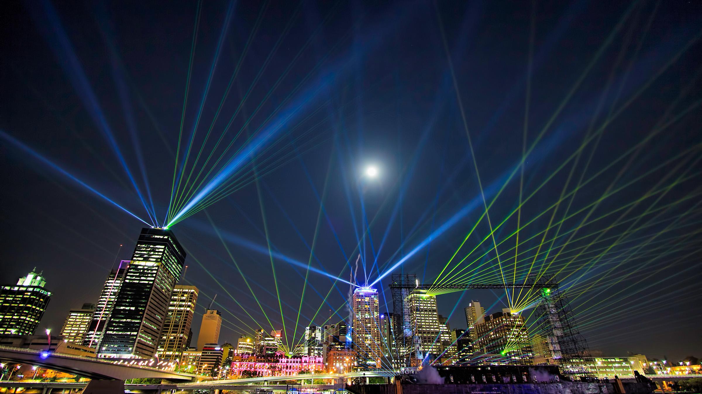Brisbane CBD skyline at night time lit up in a light show of multi-coloured lasers.