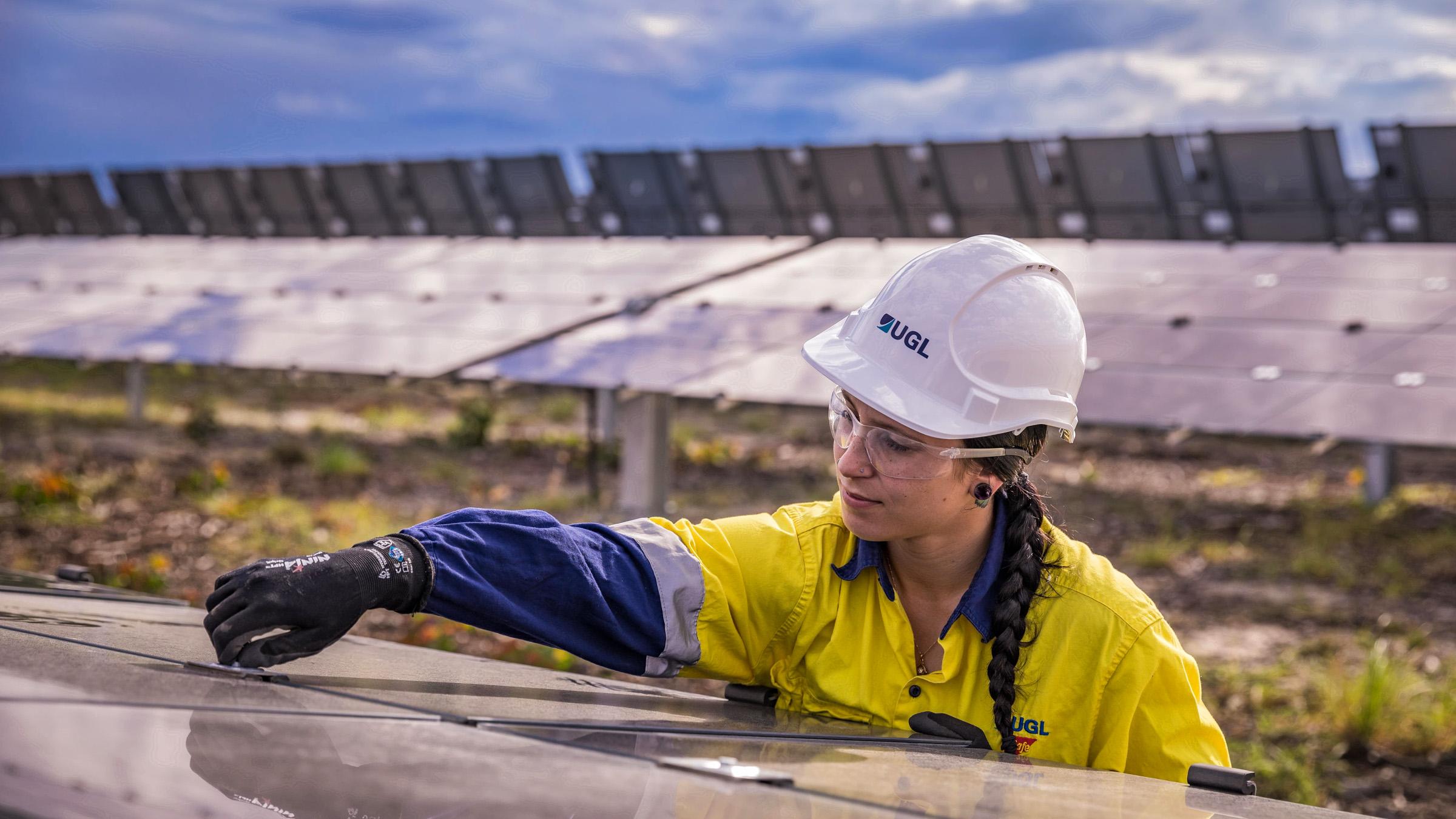 Worker, wearing high-vis and safety equipment,  maintaining a solar panel