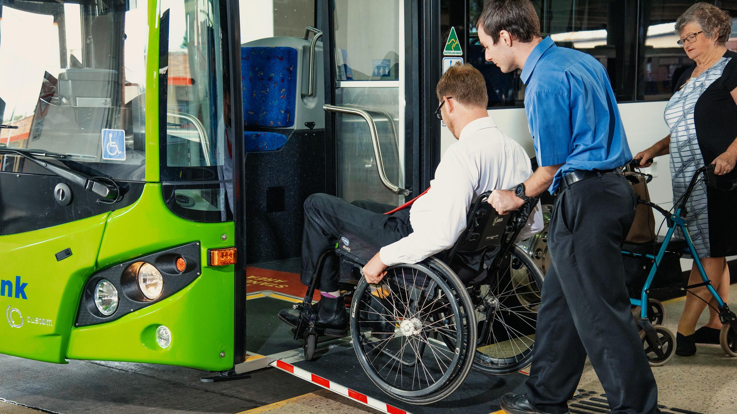 Bus driver assisting a person in a wheelchair to get onto the bus via a ramp