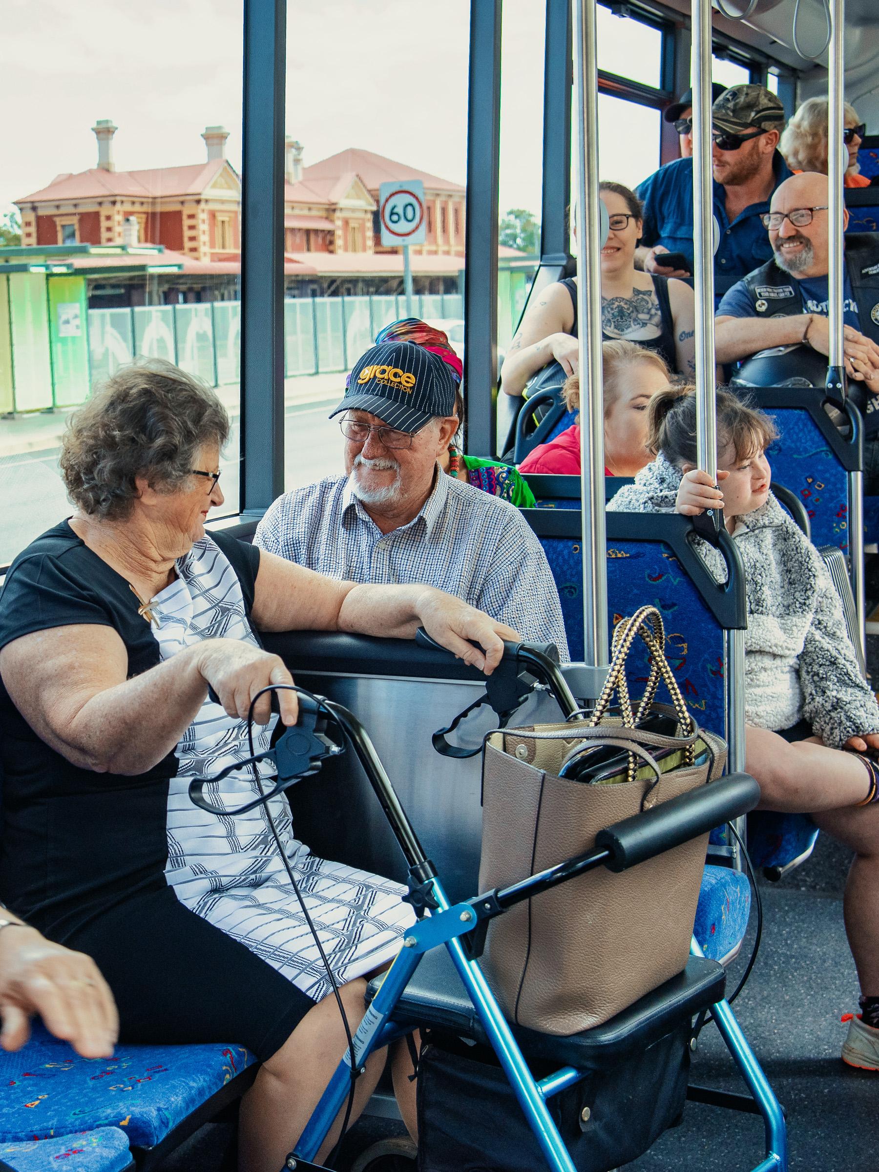 Bus passenger sitting in priority seating section with a mobility walker, smiling and talking to another passenger