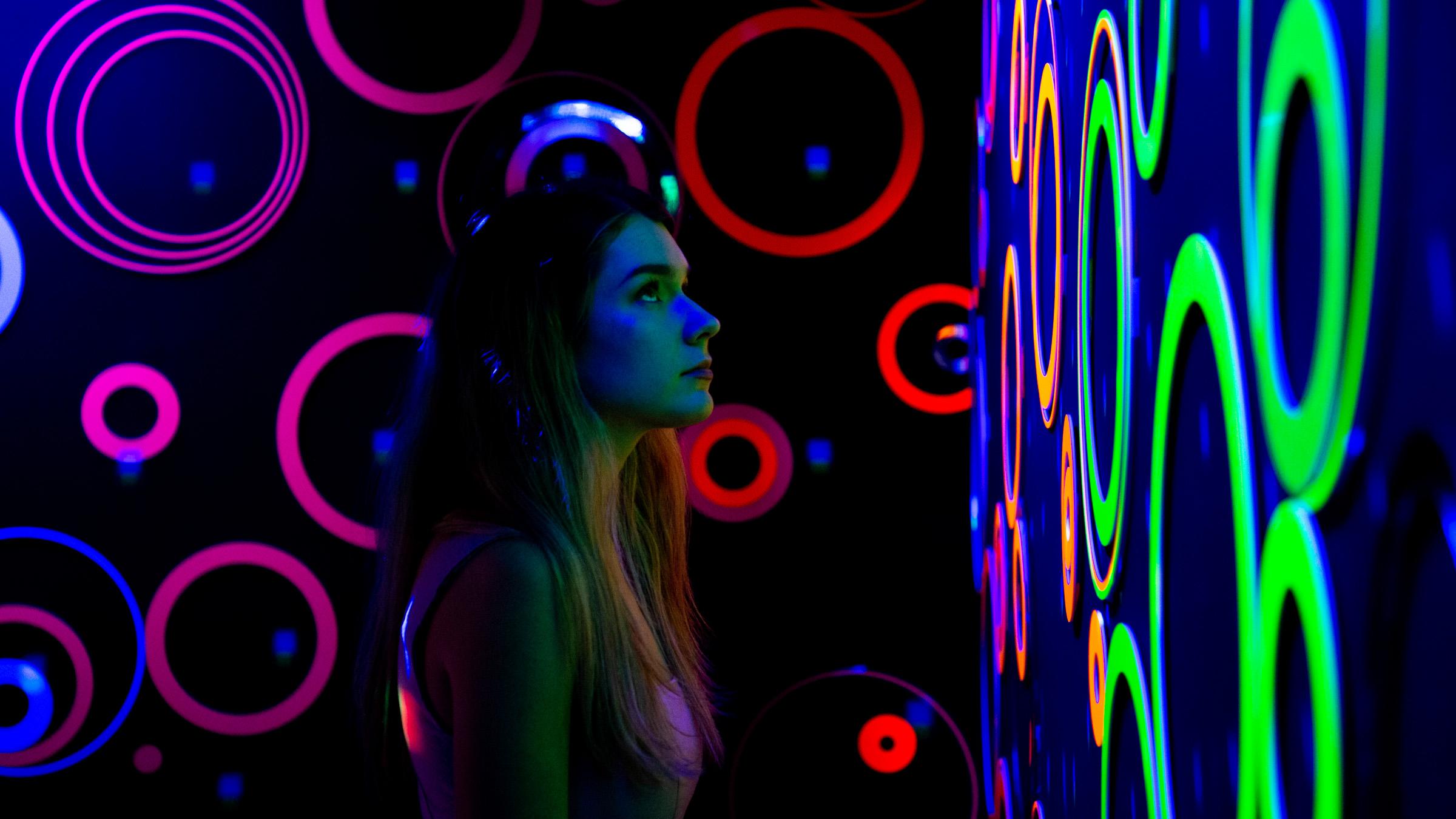 Young person in a dark room admiring glowing neon circles art on the wall