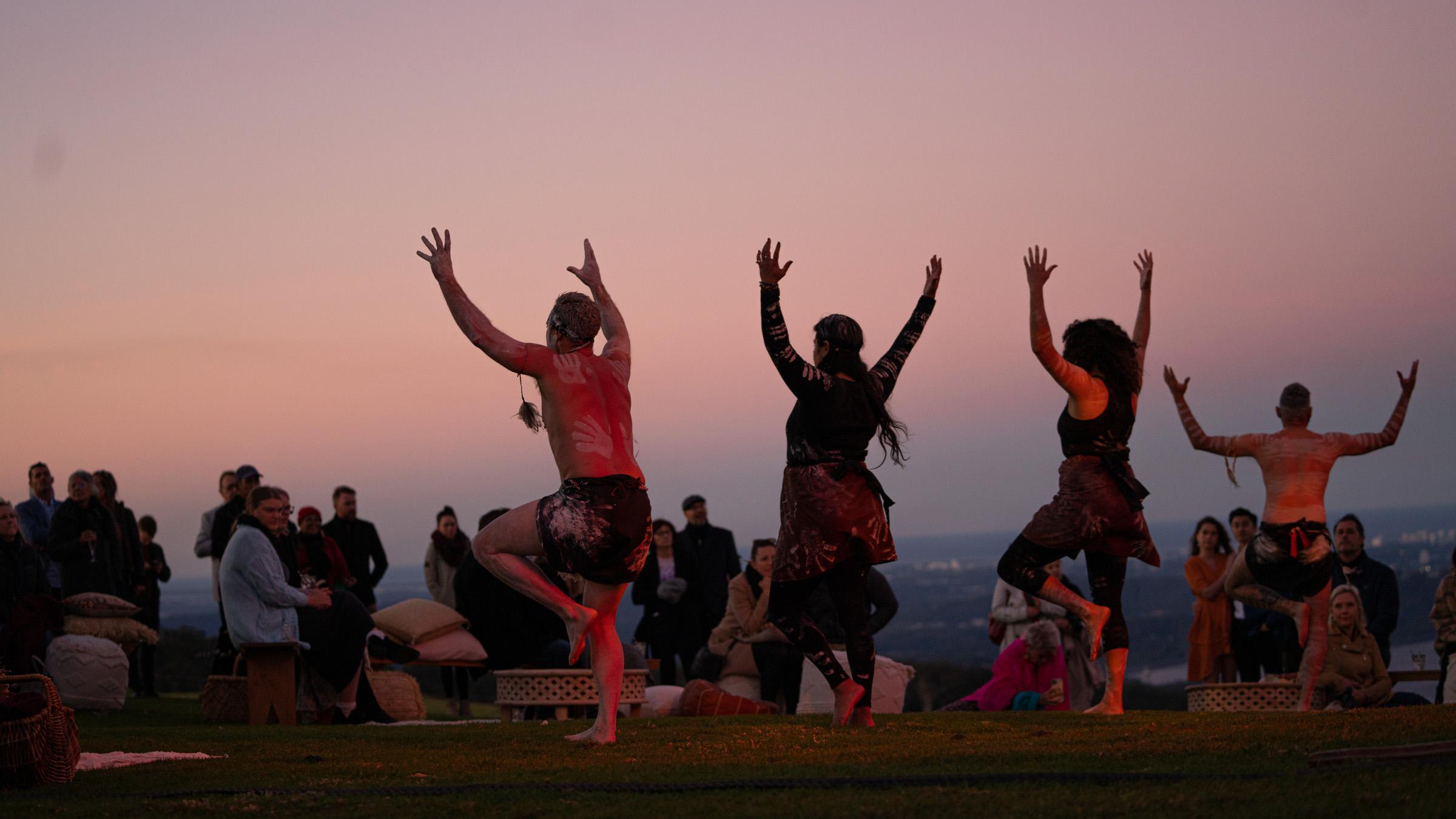 Four First Nations performers dance for an excited crowd at sunset in the Scenic Rim