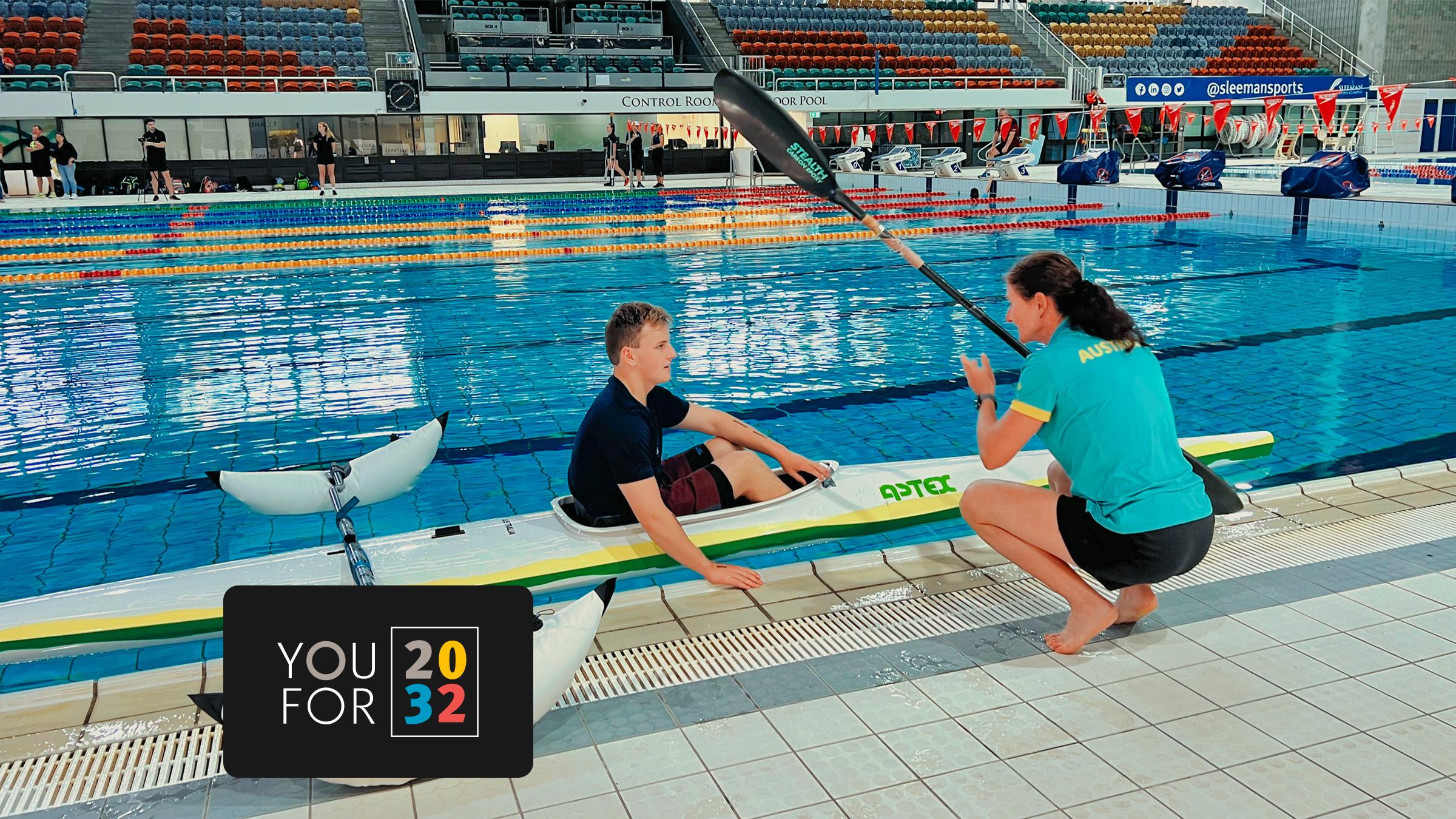 Young athlete in a kayak in an indoor pool speaking with his coach