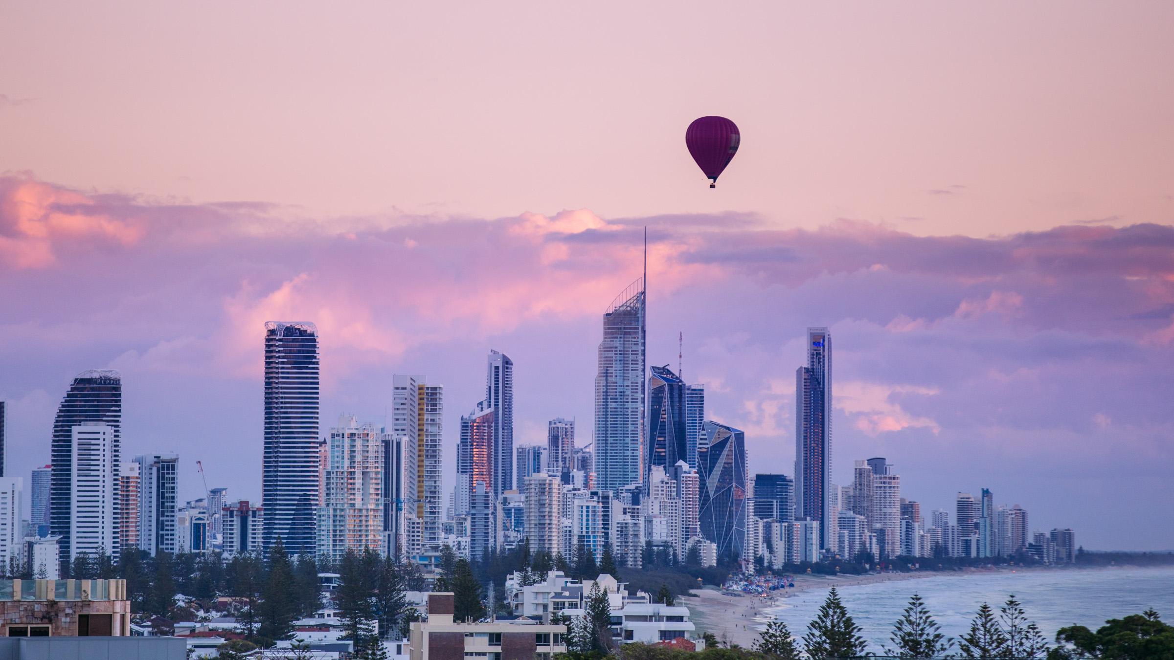 A pink and purple sunset over Surfers Paradise with a hot air balloon floating in front of the cityscape