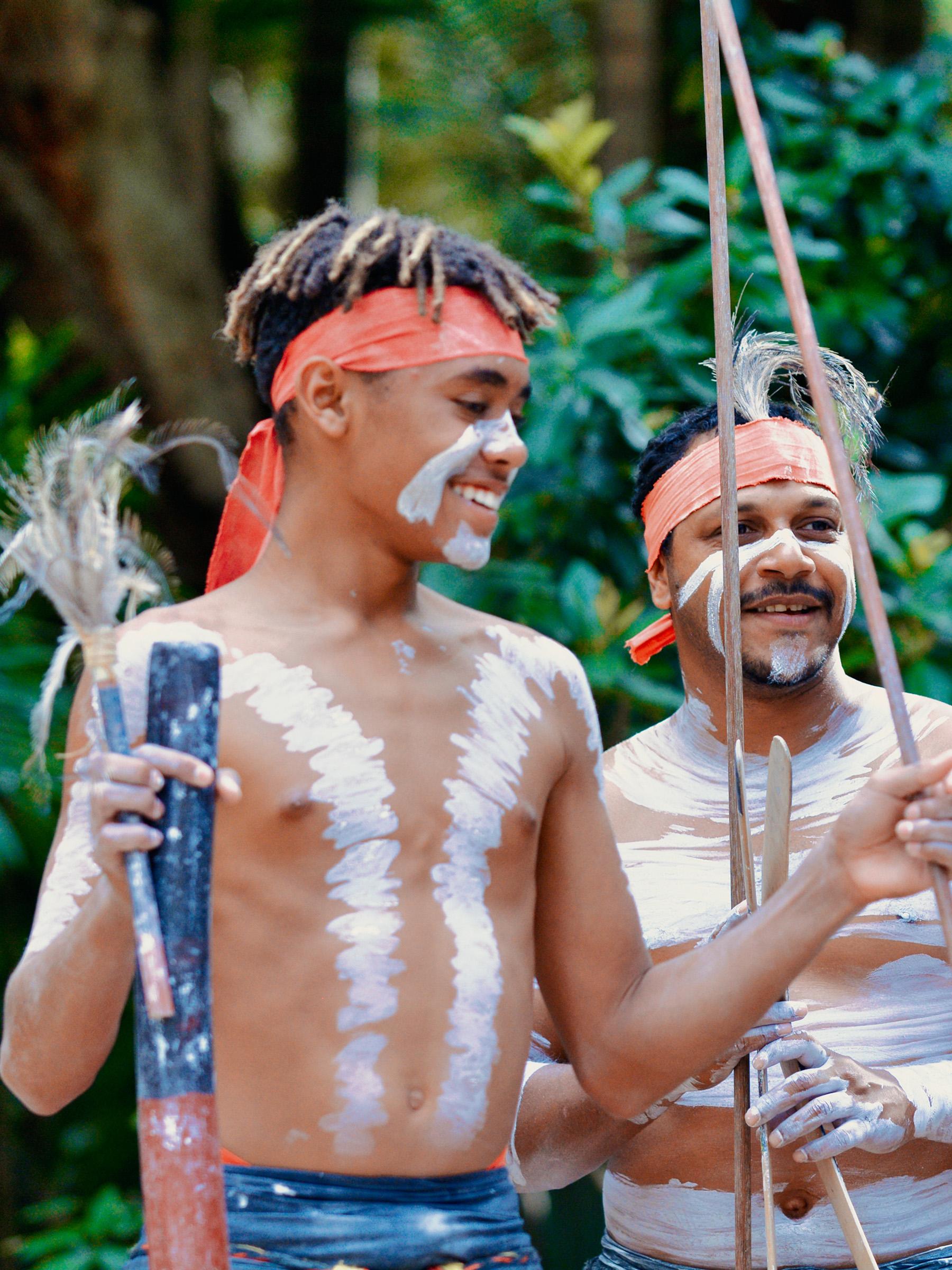 Two young First Nations men with traditional face and body paint, smiling during a performance