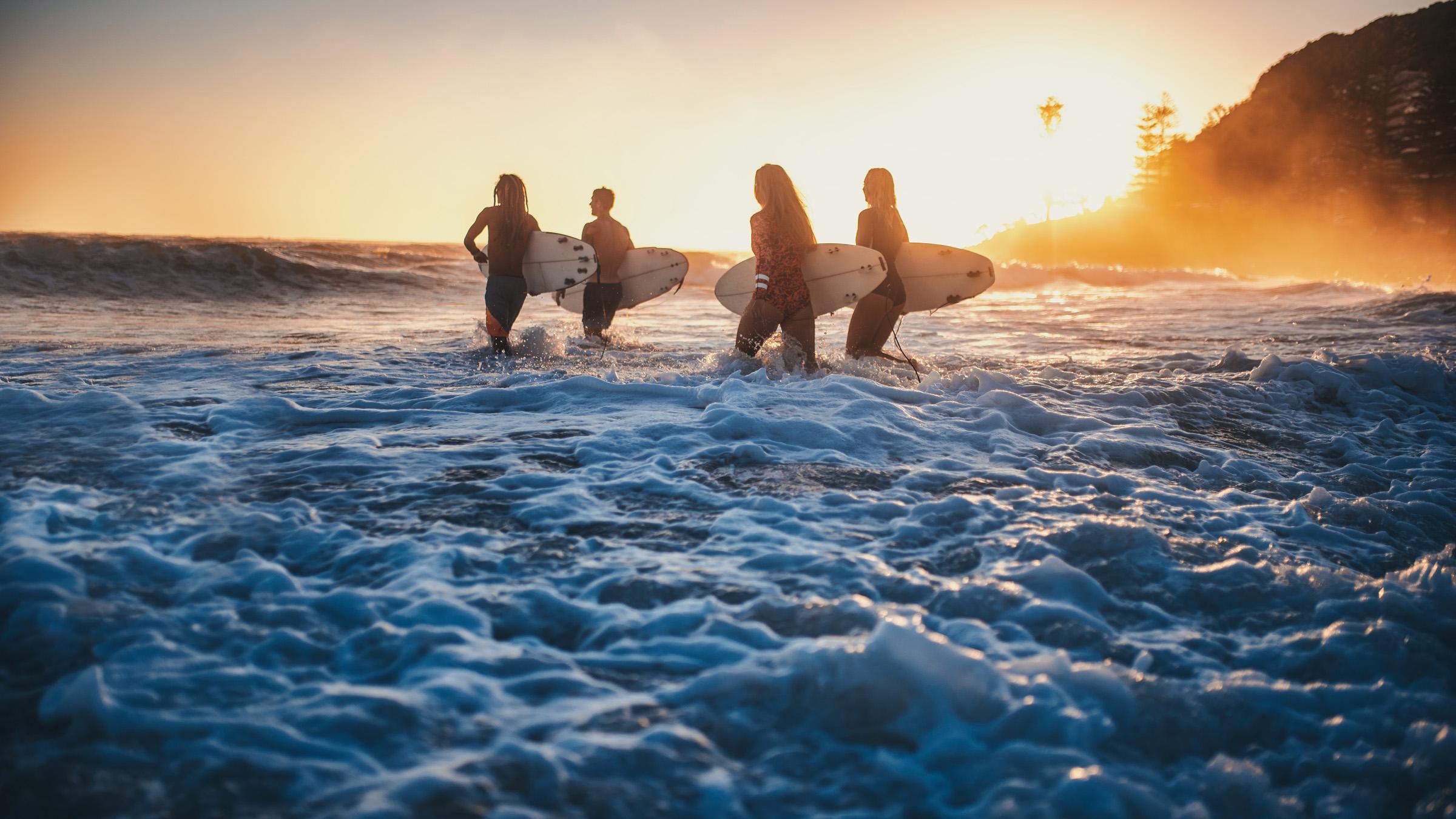 Four surfers, running into the water early in the morning with surfboards in their hands.
