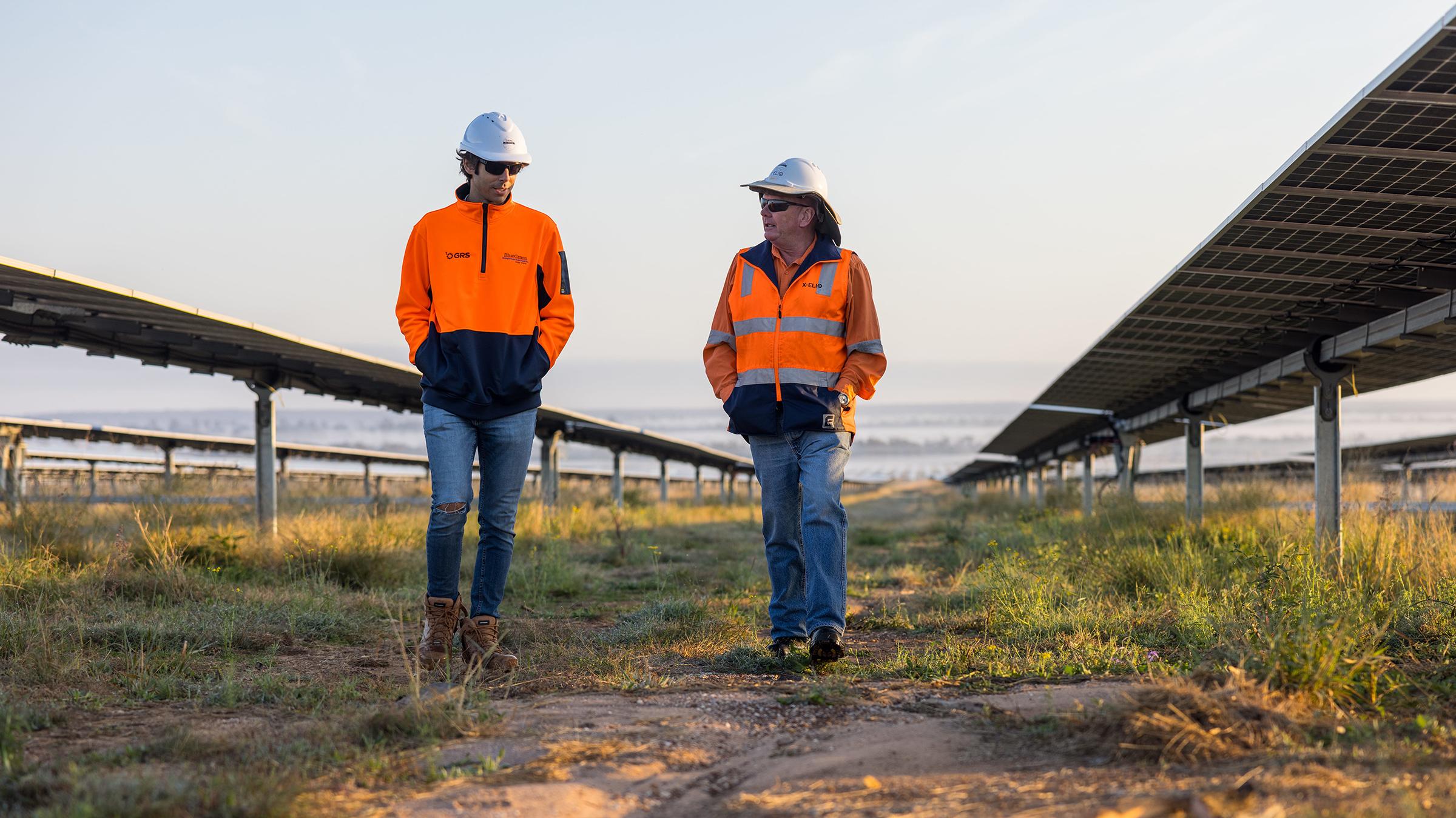 Two workers in high vis walking through Solar panel farm